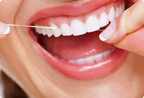 persona enseñando los dientes y limpiándolos con hilo dental